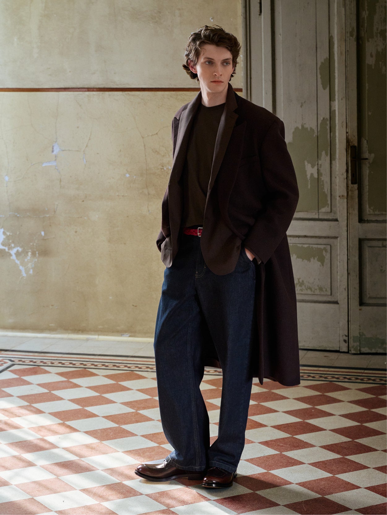 A man stands in a room with a checkered floor and peeling walls, wearing brown DERBY shoes.